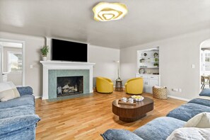 Een woonkamer met een open haard, twee gele fauteuils, een salontafel en een tv boven de open haard.
