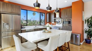 A modern kitchen with stainless steel appliances, a large island with bar stools, and a view of palm trees through the windows. - Silverlake Sunset Treehouse Art-filled Escape w/ Jacuzzi + Sauna Avantstay (Los Angeles)