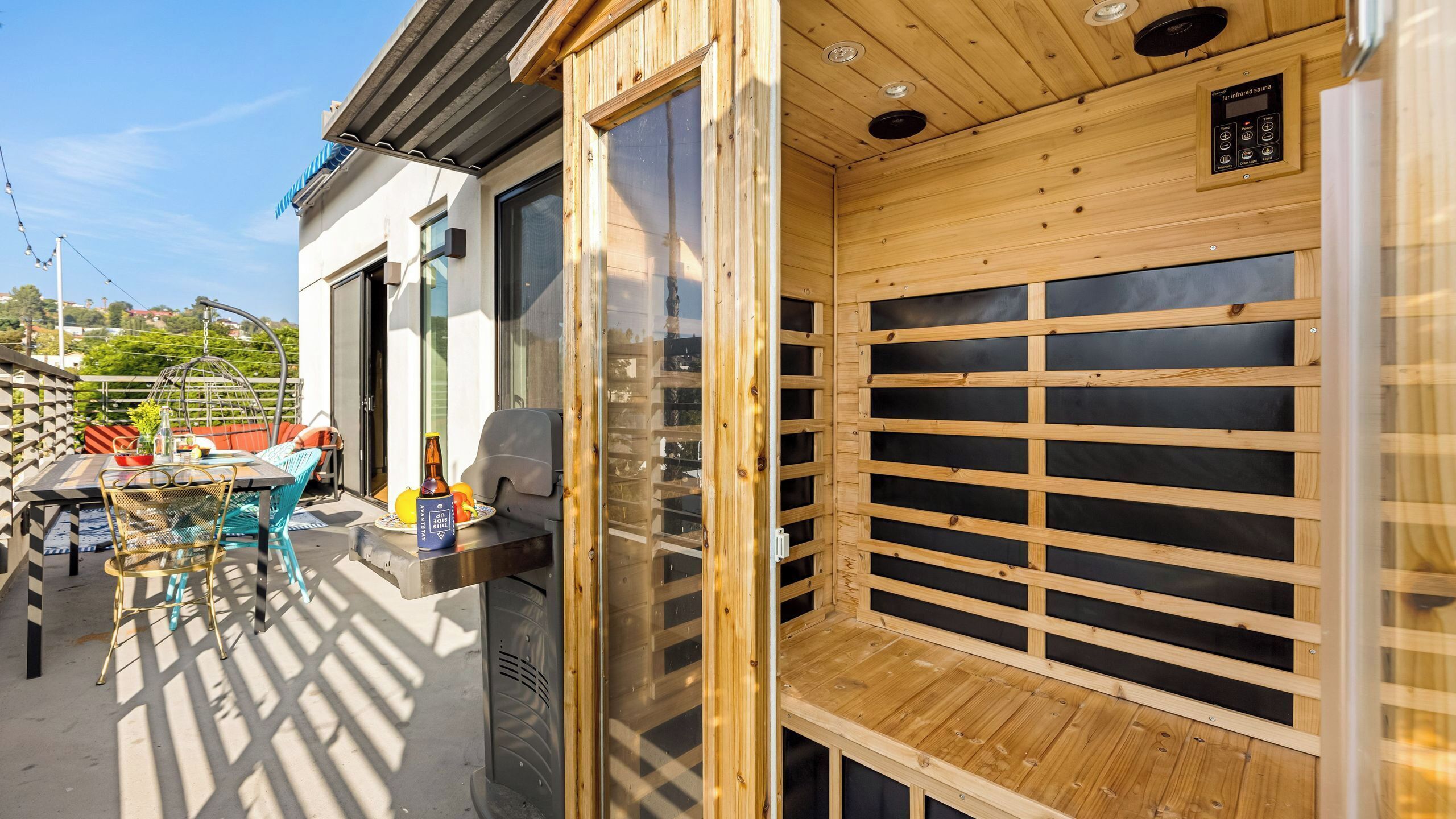 Una sauna a infrarossi con listelli di legno, un tavolo con una bottiglia e una sedia all'esterno di un edificio.