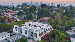 A multi-story residential building with a flat roof, surrounded by palm trees and other vegetation.