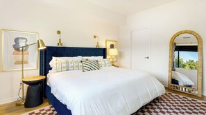Un dormitorio con una cama grande, lámparas de noche, un espejo y una obra de arte enmarcada en la pared.