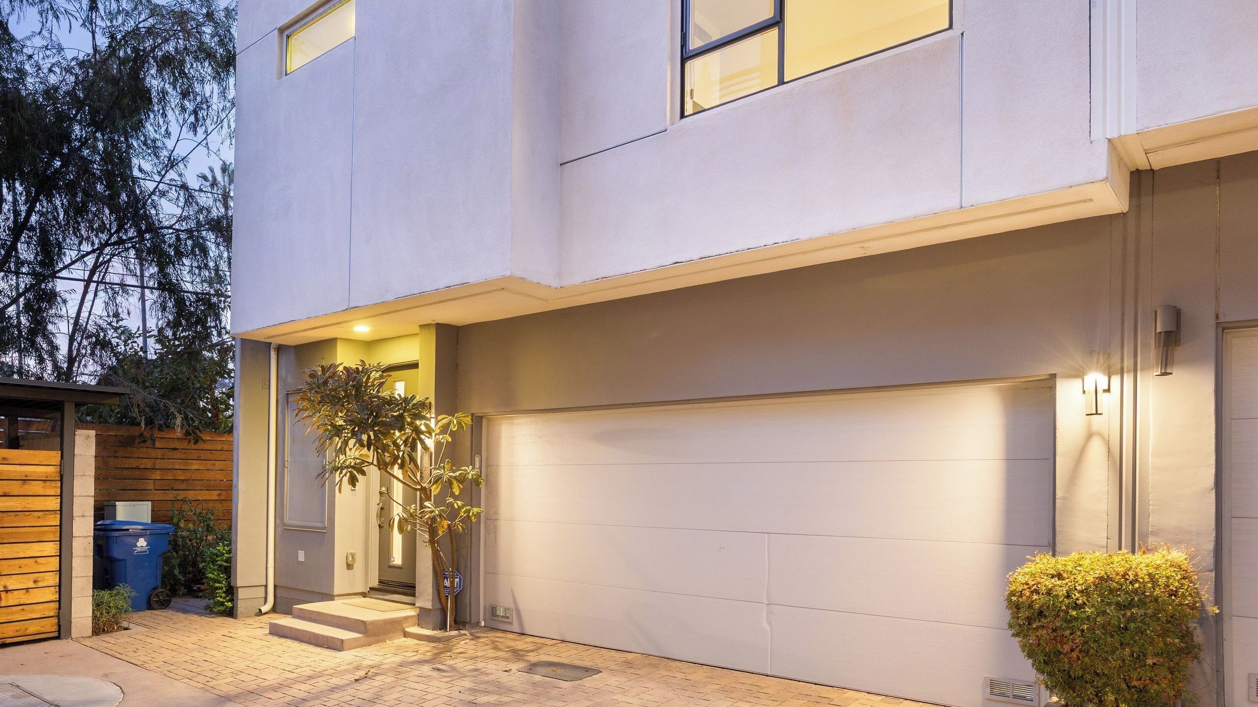 A modern two-story house with a garage, a small front yard, and a wooden fence.