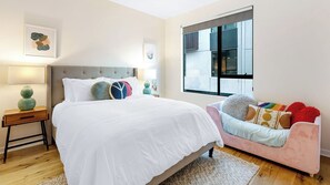 A bedroom with a bed, bedside table, lamp, and a sofa with cushions.