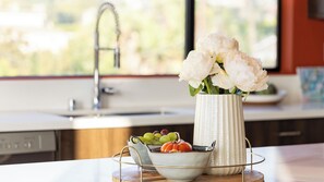 A kitchen counter with a vase of flowers, a bowl of fruit, and a sink. - Silverlake Sunset Treehouse Art-filled Escape w/ Jacuzzi + Sauna Avantstay (Los Angeles)
