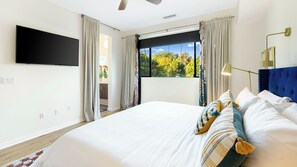 Un dormitorio con una cama grande, un televisor de pantalla plana, un ventilador de techo y una ventana con cortinas.