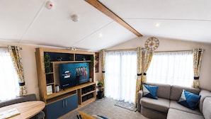 Ett modernt vardagsrum med en platt-TV, hyllor i trä, en soffa och gardiner.