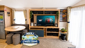 Ett modernt vardagsrum med en platt-TV, möbler i trä och en skylt för MKRJ Rentals.