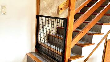 A wooden staircase with a metal safety gate, stone steps, and a white wall.