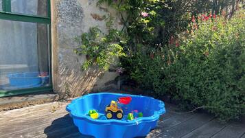 A blue plastic kiddie pool filled with toys and a small yellow toy vehicle on a wooden deck.