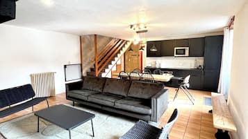 A spacious living area with a sofa, two chairs, a coffee table, and a kitchen in the background.