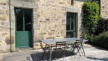 A stone building with a green door, a window, and a table with chairs outside.