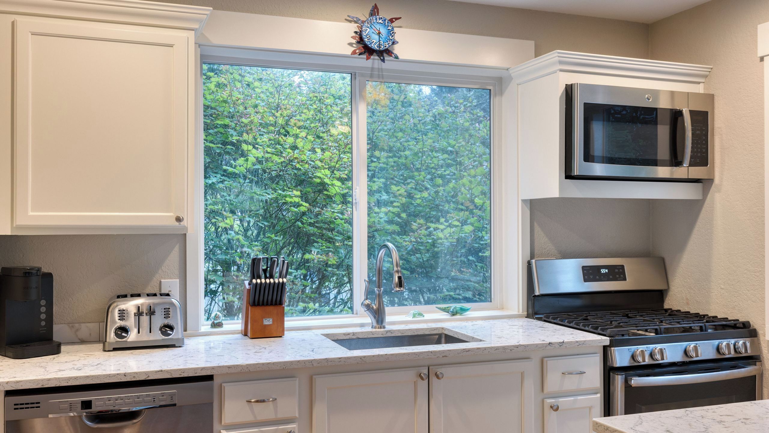 Una cocina con ventana, microondas, estufa y lavavajillas.