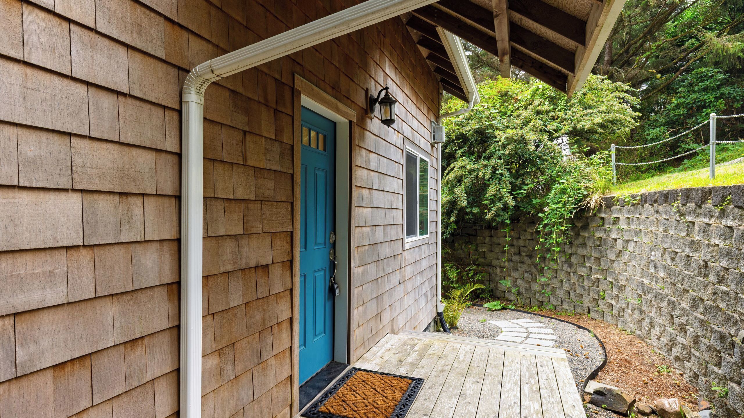 A wooden house with a blue door, a porch, and a stone wall.