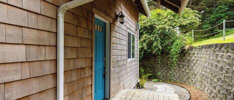 A wooden house with a blue door, a porch, and a stone wall.