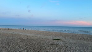 Una playa de guijarros con una valla de madera y cielo despejado.