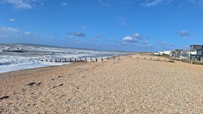 A pebbled beach with a wooden walkway, houses in the background, and the sea. - Mkrj Premium - Parkdean Camber Sands - (Rye)