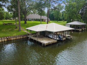 A docked boat with a covered area, a grassy area with a bench, and a house in the background. - Welcome to Lake Blessing 2026 (Frankston)