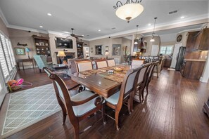 A spacious dining area with a wooden table and chairs, a television, and a kitchen in the background. - Welcome to Lake Blessing 2026 (Frankston)