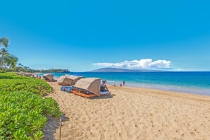 A beach with several covered seating areas, a clear blue sky, and a distant mountain. - Beachfront Ka'anapali Studio - Vacation West Maui (Lahaina)