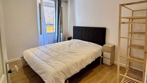 A bedroom with a bed, a wooden floor, a nightstand, a bedside table, and a window with curtains. - Casa Mare Lina Île rousse - T3 old town 1 min from the beach (L'Île-Rousse)