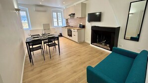 A modern living room with a fireplace, a dining area with a table and chairs, and a kitchen with a TV above the counter. - Casa Mare Lina Île rousse - T3 old town 1 min from the beach (L'Île-Rousse)