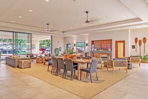 A spacious lobby with a wooden dining table, comfortable seating, and a large window offering a view of the street. - Valley Isle Resort #506 - Vacation West Maui (Lahaina)