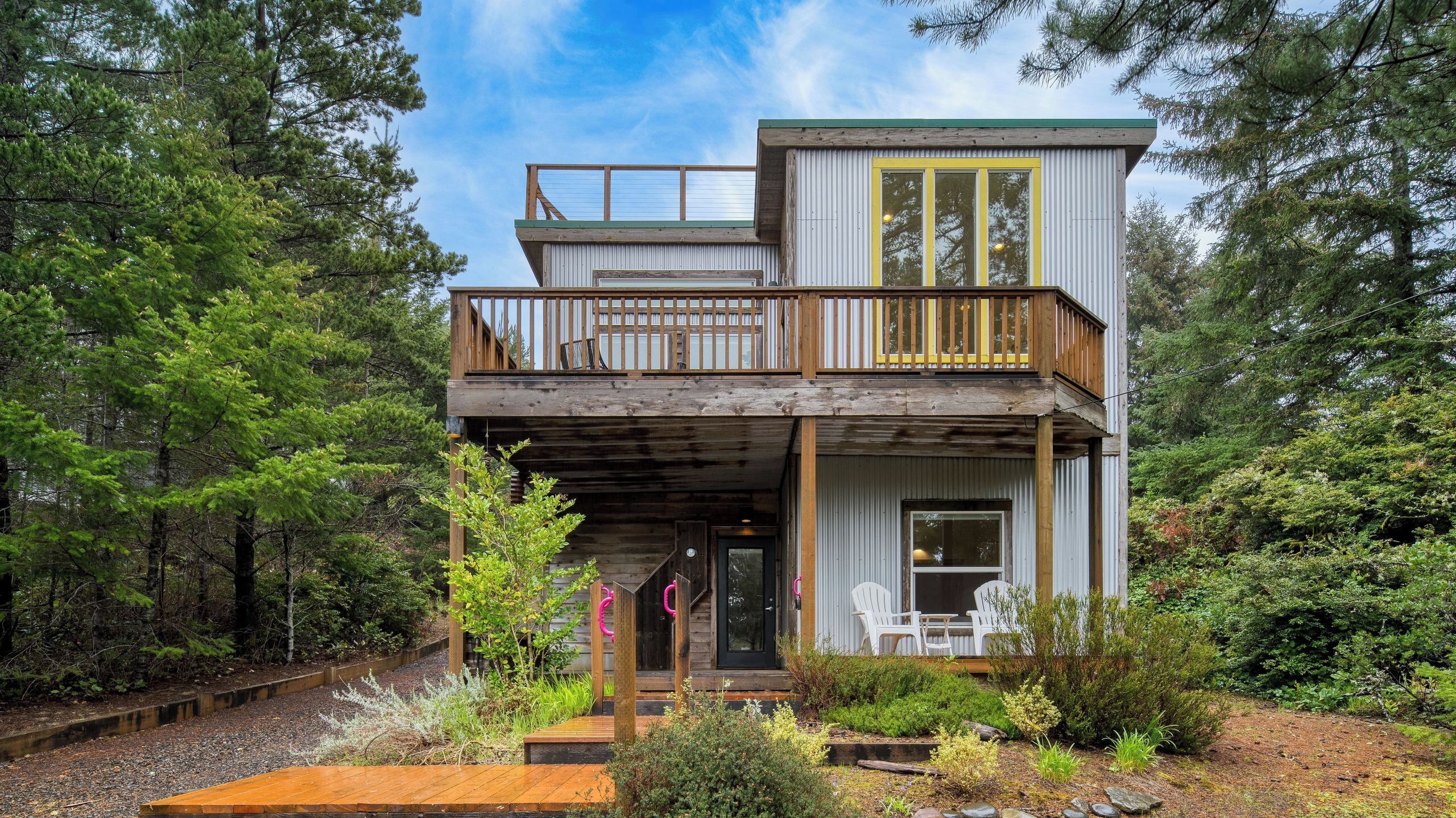 A two-story cabin with a wooden deck, a balcony, and a front porch with outdoor seating.