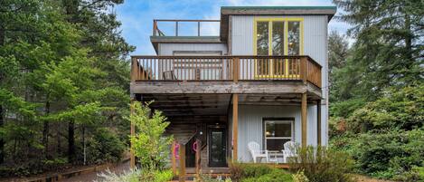 A two-story cabin with a wooden deck, a balcony, and a front porch with outdoor seating.