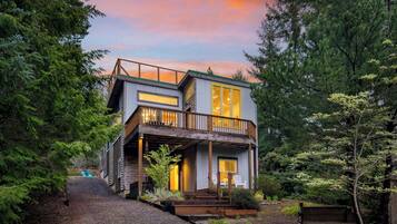 A two-story wooden cabin with a balcony, surrounded by dense forest.