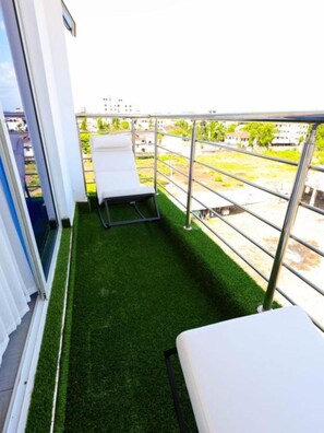 A balcony with artificial grass, a white chair, and a metal railing. - 5 Minutes to the Beach | Stylish 1-Bedroom Apartment in Mombasa (Mombasa)