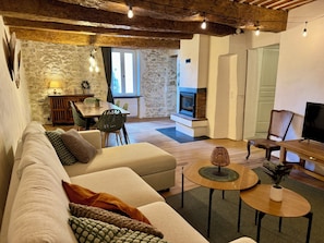 Un salon chaleureux avec un mur en pierre, une cheminée, un coin repas et un téléviseur.