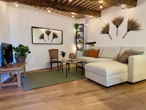 Un salon comprenant un canapé, une table basse en bois, un fauteuil, une petite table avec une lampe, un tableau encadré et une bibliothèque.
