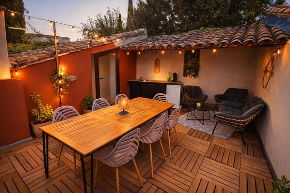A patio with a wooden table and chairs, a small kitchen area, and outdoor seating.