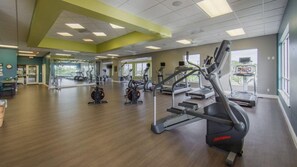 Un'ampia palestra con macchinari cardio, specchi e pavimento in legno.