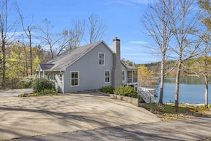 A single-story house with a chimney, a driveway, and a dock extending into a lake.