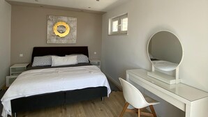 Une chambre à coucher comprenant un lit, des tables de chevet, un bureau avec une chaise, un miroir et une œuvre d’art murale.