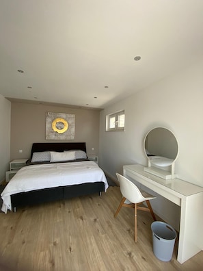 Ein Schlafzimmer mit Bett, Nachttischen, einem Schreibtisch mit Stuhl, einem Spiegel und einem Wandbild.