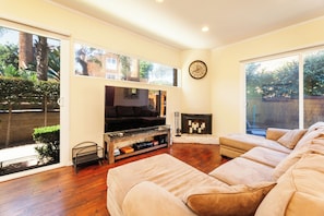 Ein Wohnzimmer mit Fernseher, Sofa, Kamin und großen Fenstern.