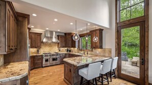 A spacious kitchen with wooden cabinets, a large island with bar stools, stainless steel appliances, and a view through a glass door. - Luxury West Vail Duplex - Multi-Level Living Areas (Vail)