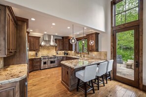 A spacious kitchen with wooden cabinets, a large island with bar stools, stainless steel appliances, and a view through a glass door. - Luxury West Vail Duplex - Multi-Level Living Areas (Vail)