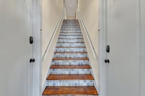 Eine Treppe mit gemusterten Fliesen und Holzdielen, gesäumt von weißen Türen mit schwarzen Griffen.
