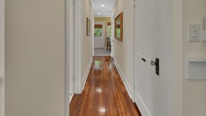 Un couloir doté d’un plancher en bois, de portes blanches et d’une vue sur une pièce dont le sol est recouvert de carreaux.