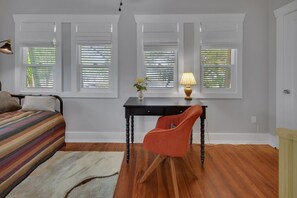 Ein Schlafzimmer mit Bett, Schreibtisch mit Stuhl und einem Fenster mit Jalousien.