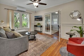 Ein Wohnzimmer mit einer Couch, einem kleinen Tisch, einem roten Sessel, einem Deckenventilator und Blick durch eine Glastür.
