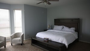 Une chambre à coucher comprenant un lit, un ventilateur de plafond, une table de chevet, une lampe et deux chaises.