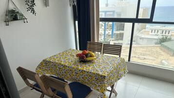 Et spiseområde med et bord dækket af en gul og hvid ternet dug, træstole med blå hynder og en skål med frugt på bordet.