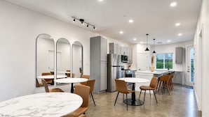 A modern kitchen with white cabinets, a stainless steel refrigerator, and a dining area with round tables and chairs. - Bishop Arts 6BR/6BA townhouse, sleeps 12, parking (Dallas)