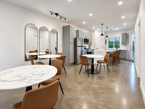A modern kitchen with white cabinets, a stainless steel refrigerator, and a dining area with round tables and chairs. - Bishop Arts 6BR/6BA townhouse, sleeps 12, parking (Dallas)