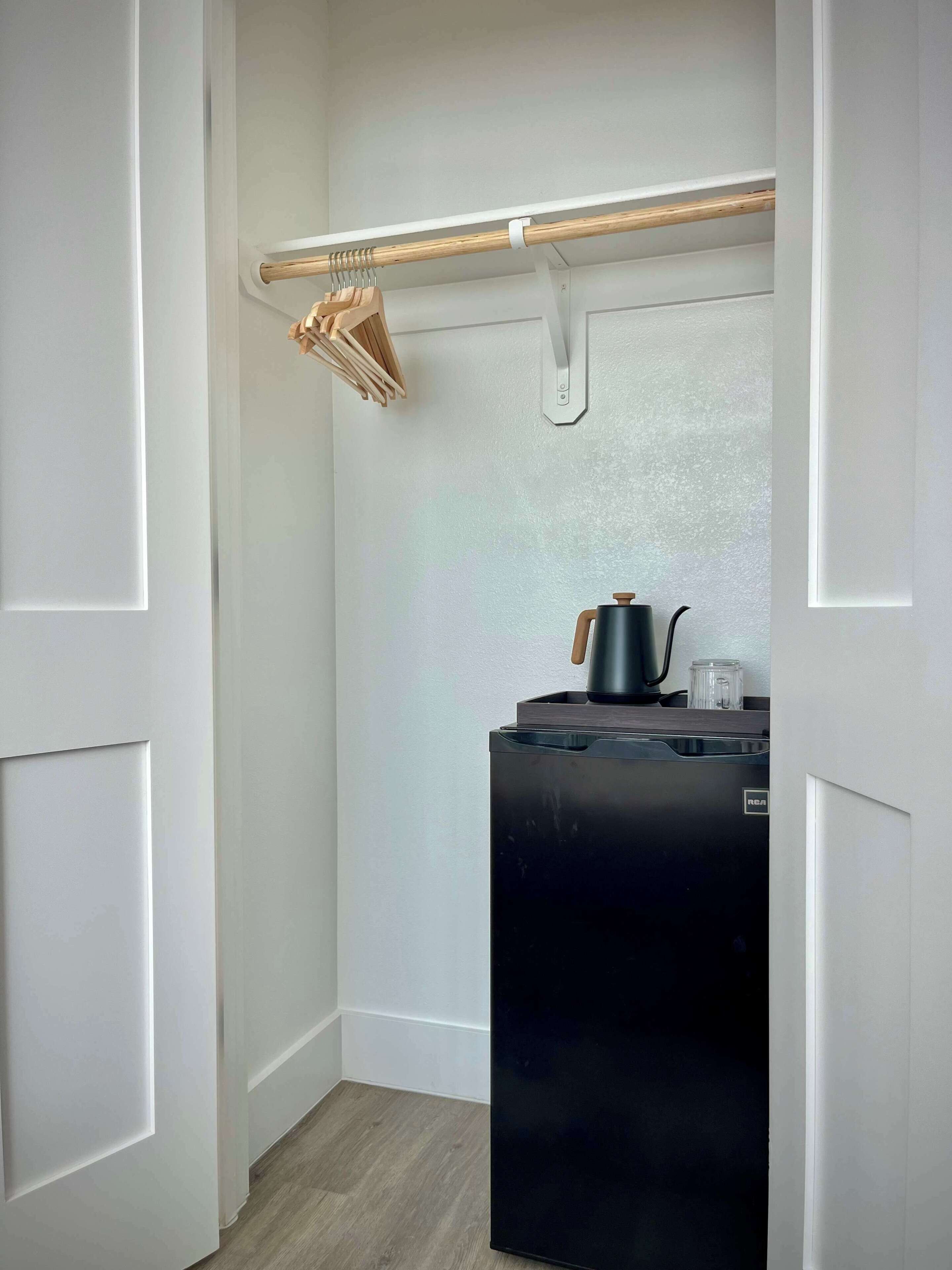 Cocina compacta con refrigerador negro, un tendedero de madera y una pequeña encimera con hervidor.