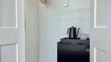 Cocina compacta con refrigerador negro, un tendedero de madera y una pequeña encimera con hervidor.